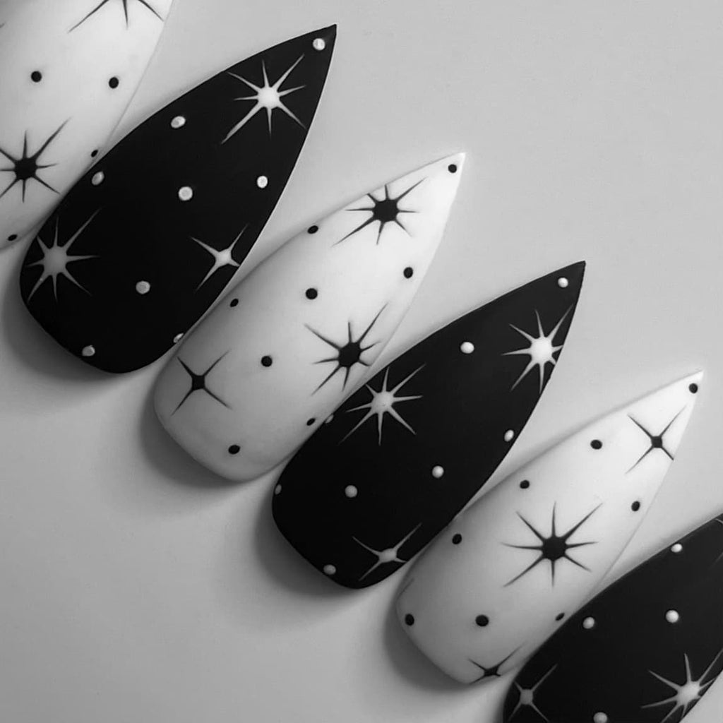 Mix of long stiletto nails with a black and white matte base. A star and dot pattern can be seen throughout the nails.