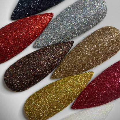 Close-up of sugar glitter nails in varying colors: blue-black, red, holographic silver, holographic brown, pale gold, yellow gold, pink, and white. 